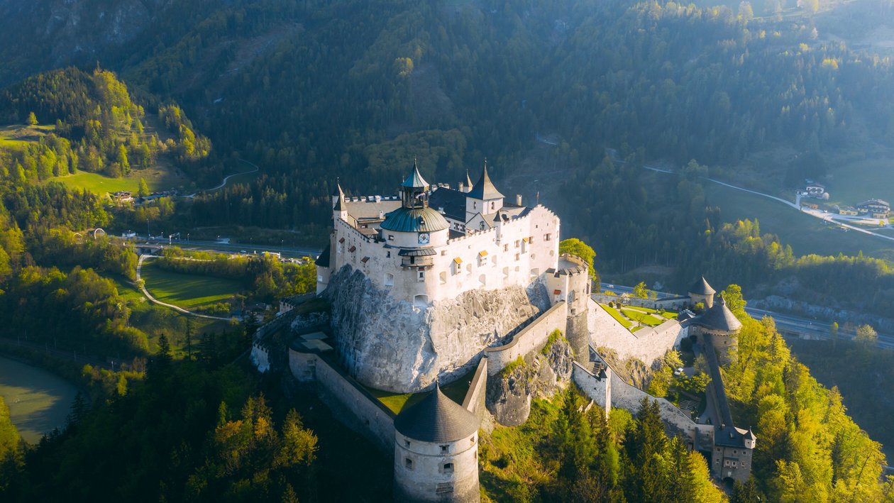 Majestätische Burg inmitten der Natur Luftaufnahme einer großen Burg auf einem Felsen, umgeben von Wäldern und Bergen.