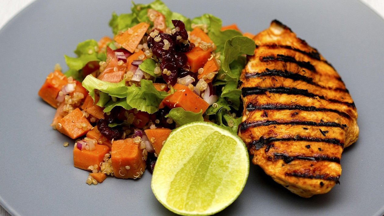 Gesunde Mahlzeit mit gegrilltem Hähnchen Ein Teller mit gegrilltem Hähnchen und einer bunten Salatmischung, garniert mit einer Limettenhälfte.