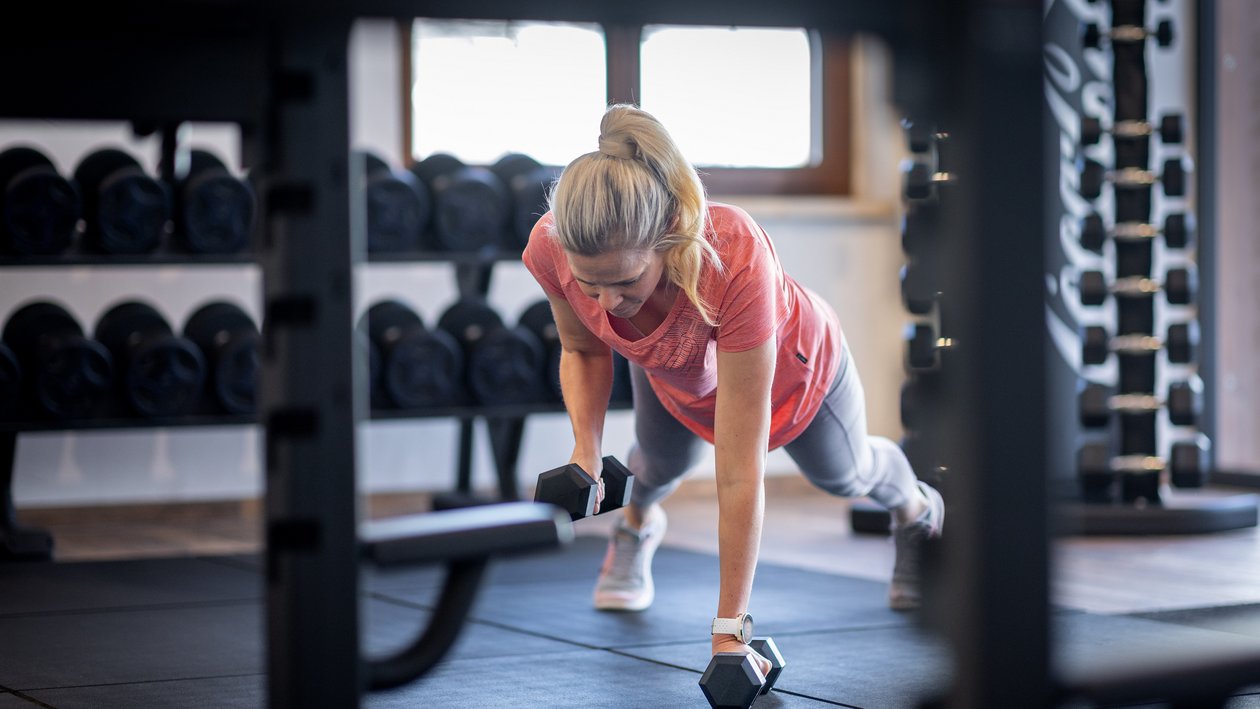 Strength training session A woman performing a plank exercise with dumbbells in a gym environment while focusing on fitness and strength.