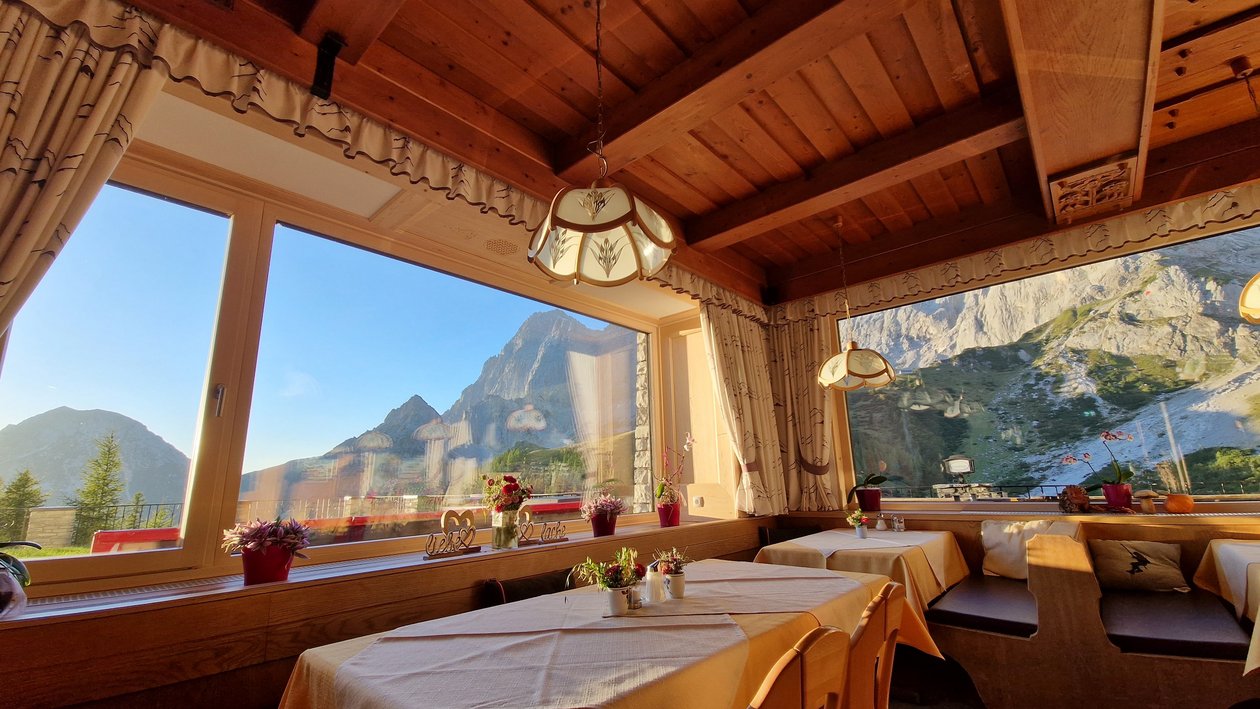Restaurant interior featuring wooden decor and tables set for dining with large windows showcasing mountains