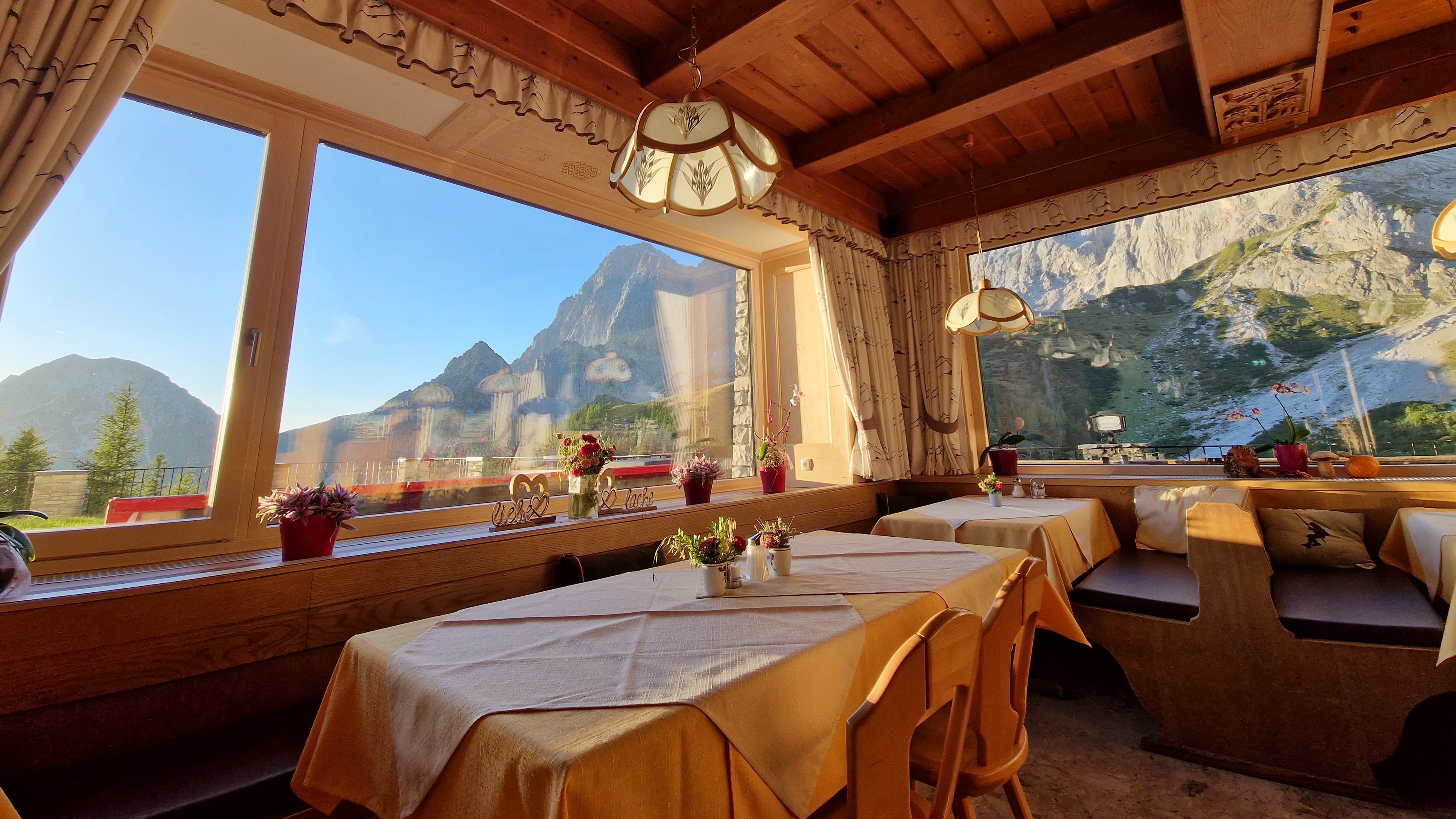 Restaurantinterior mit Holzmobiliar, Tischen und großen Fenstern zur Berglandschaft