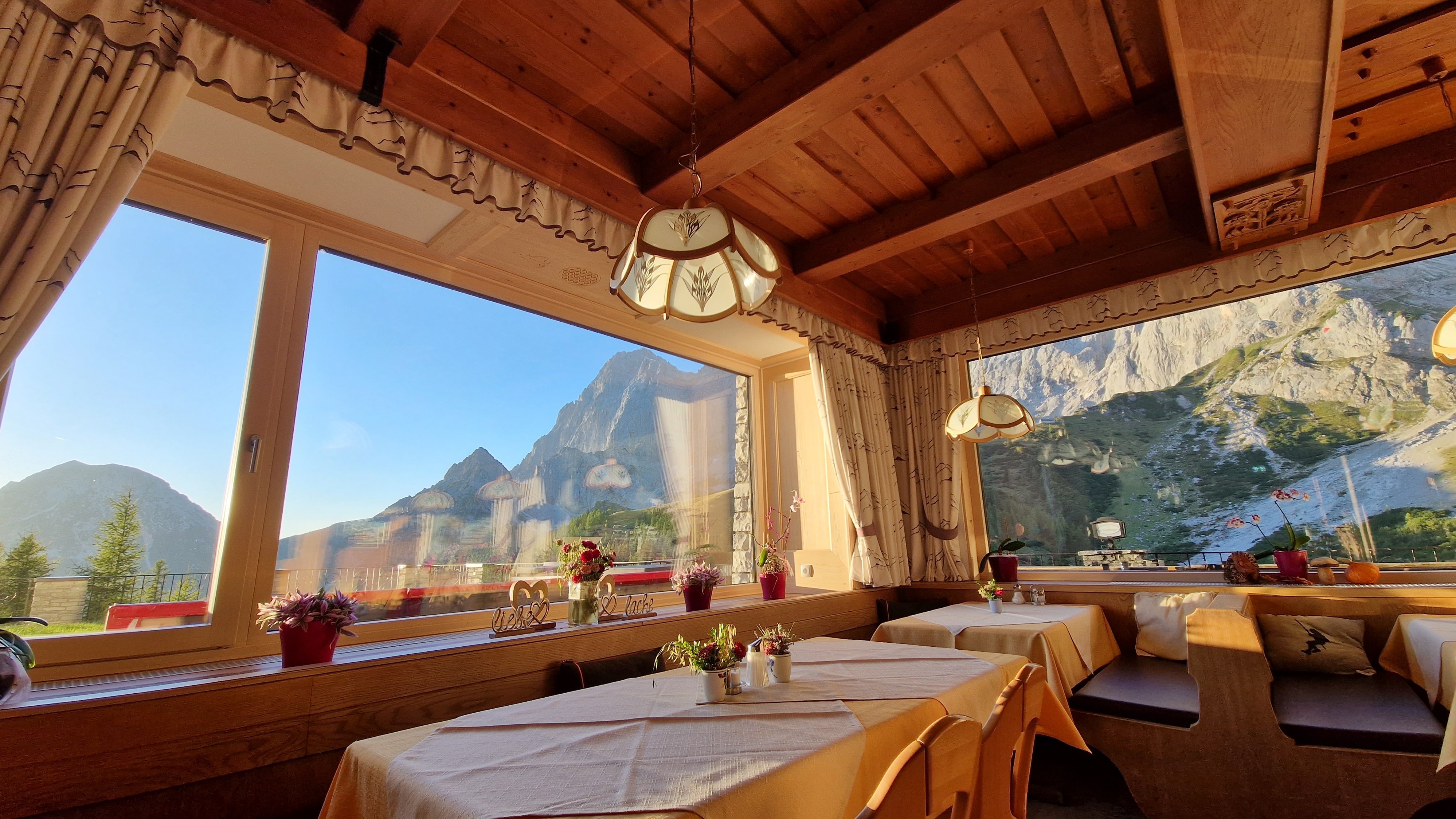 Restaurantinterior mit Holzmobiliar, Tischen und großen Fenstern zur Berglandschaft