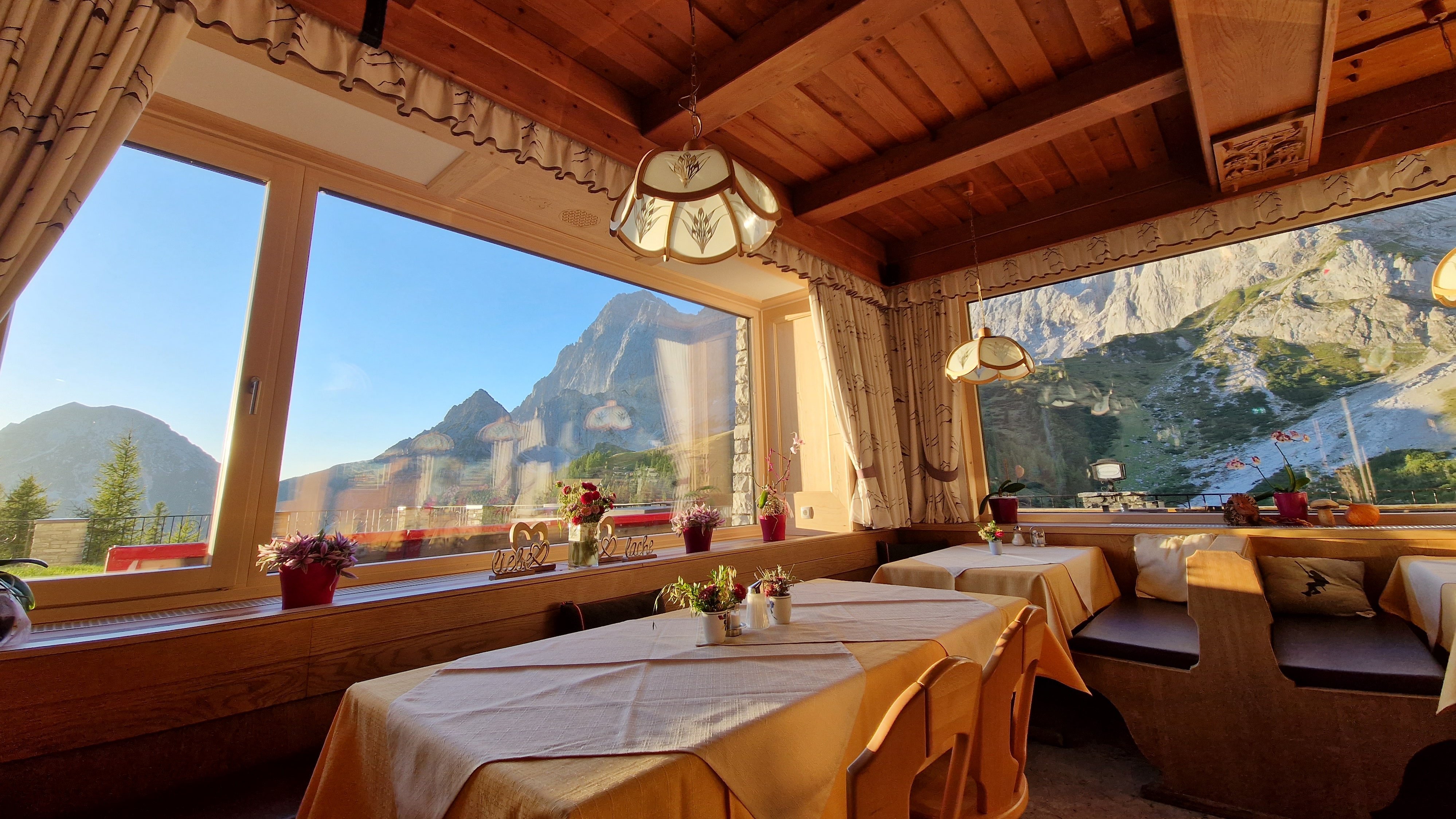 Gemütliche Stube mit Bergblick Restaurantinterior mit Holzmobiliar, Tischen und großen Fenstern zur Berglandschaft