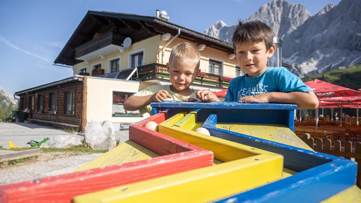 Spielende Kinder im Freien Zwei Kinder spielen mit bunten Holzspielzeugen vor Berglandschaft und einem Gebäude