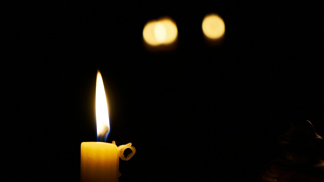 A lit candle with a bright flame illuminating a dark background, creating a serene setting.