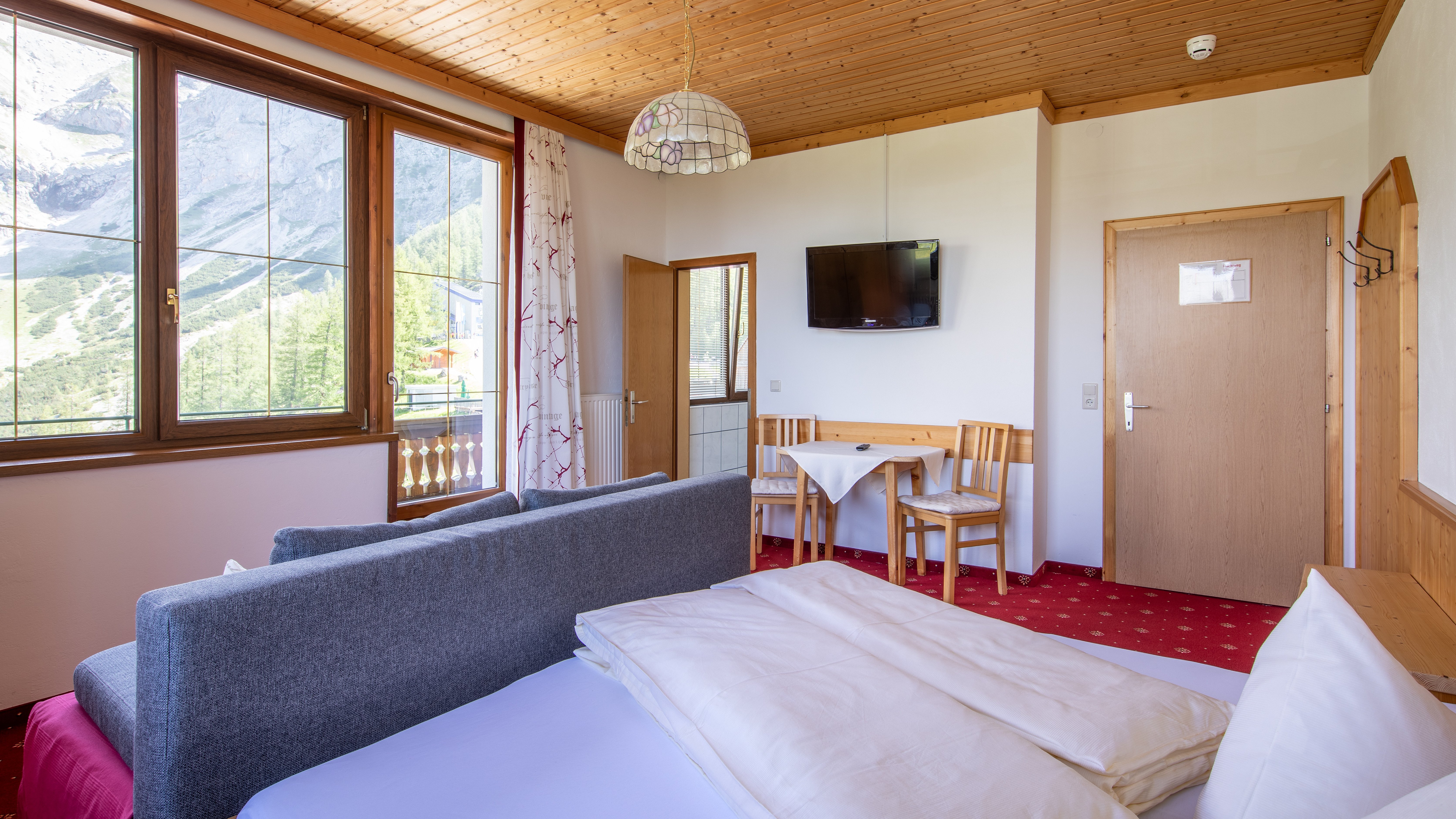 Helle Hotelzimmer mit Bett, Sitzbereich und Tisch sowie großen Fenstern zur Bergsicht
