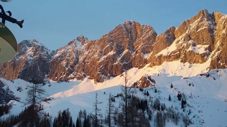 Schneebedeckte Berge mit sonnigen Felsen und einem Eingangsschild im Vordergrund