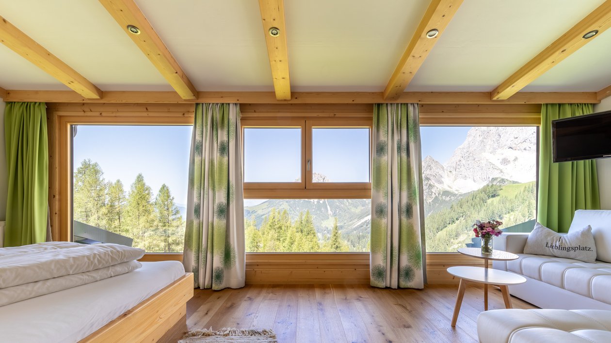 Gemütliches Chalet mit Bergblick Heller Wohnraum in einem modernen Holzhaus mit Blick auf Berge und Bäume durch große Fenster.