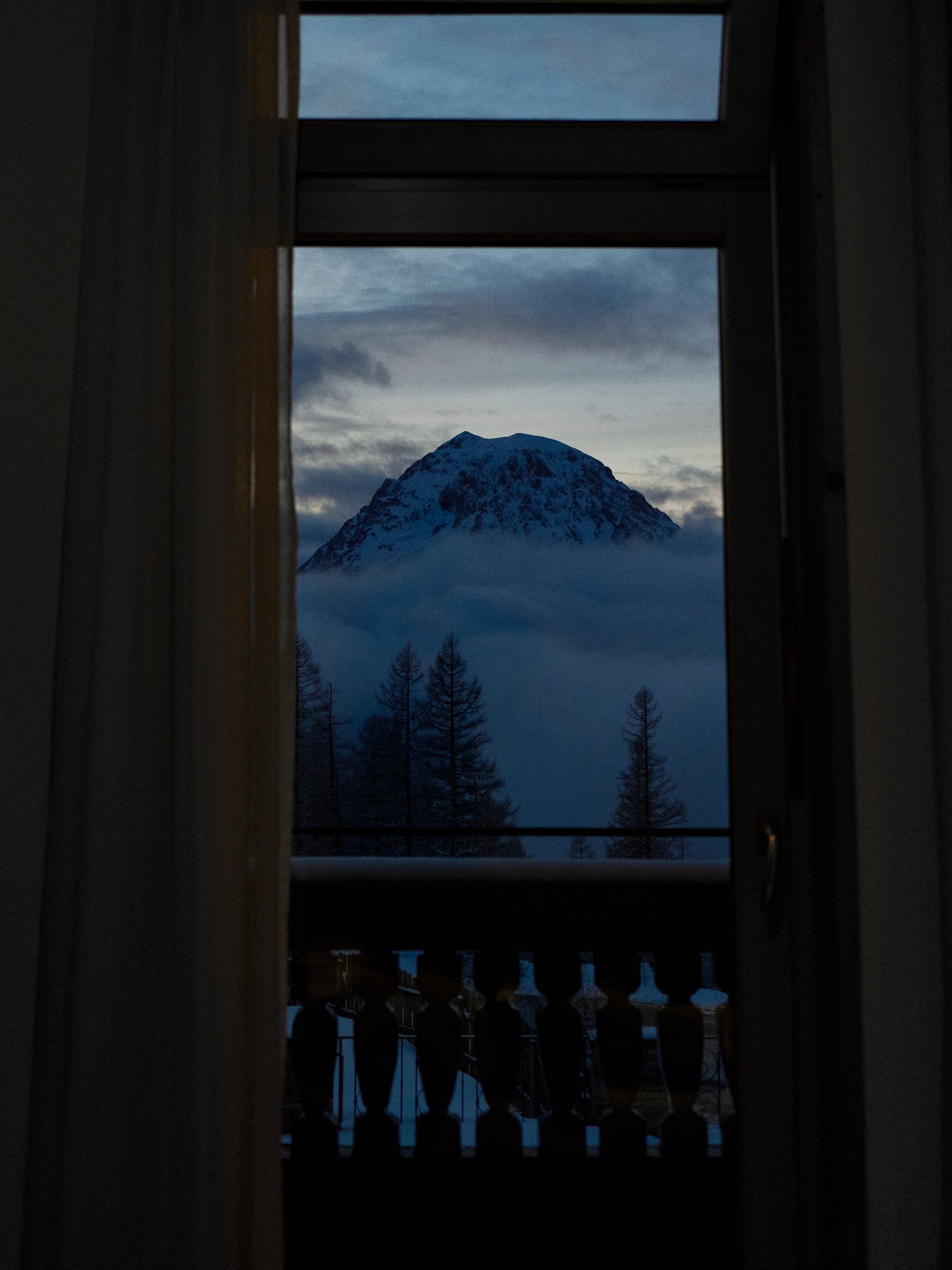 Aussicht auf schneebedeckte Berge durch ein Fenster mit Wolken im Hintergrund und einer natürlichen Landschaft.
