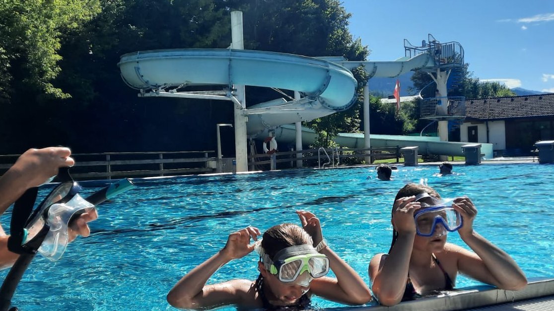 Group of children swimming in a pool with snorkeling gear and a water slide in the background