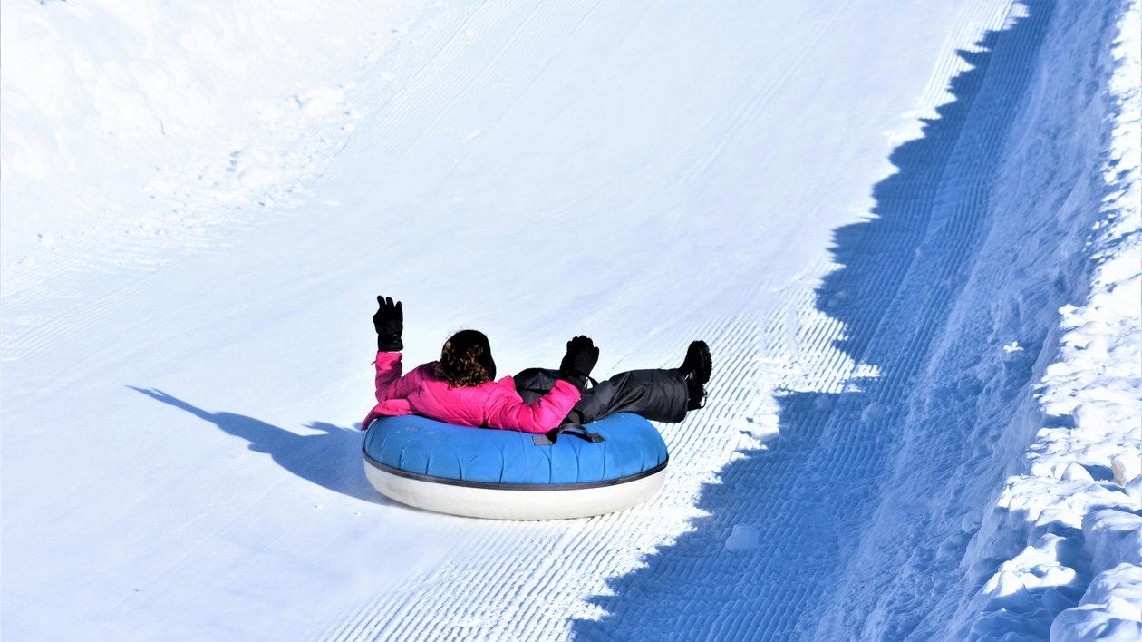 Rutschvergnügen auf der Schneepiste Person in pinker Jacke rutscht auf einem blauen Tubes einen verschneiten Hang hinunter.