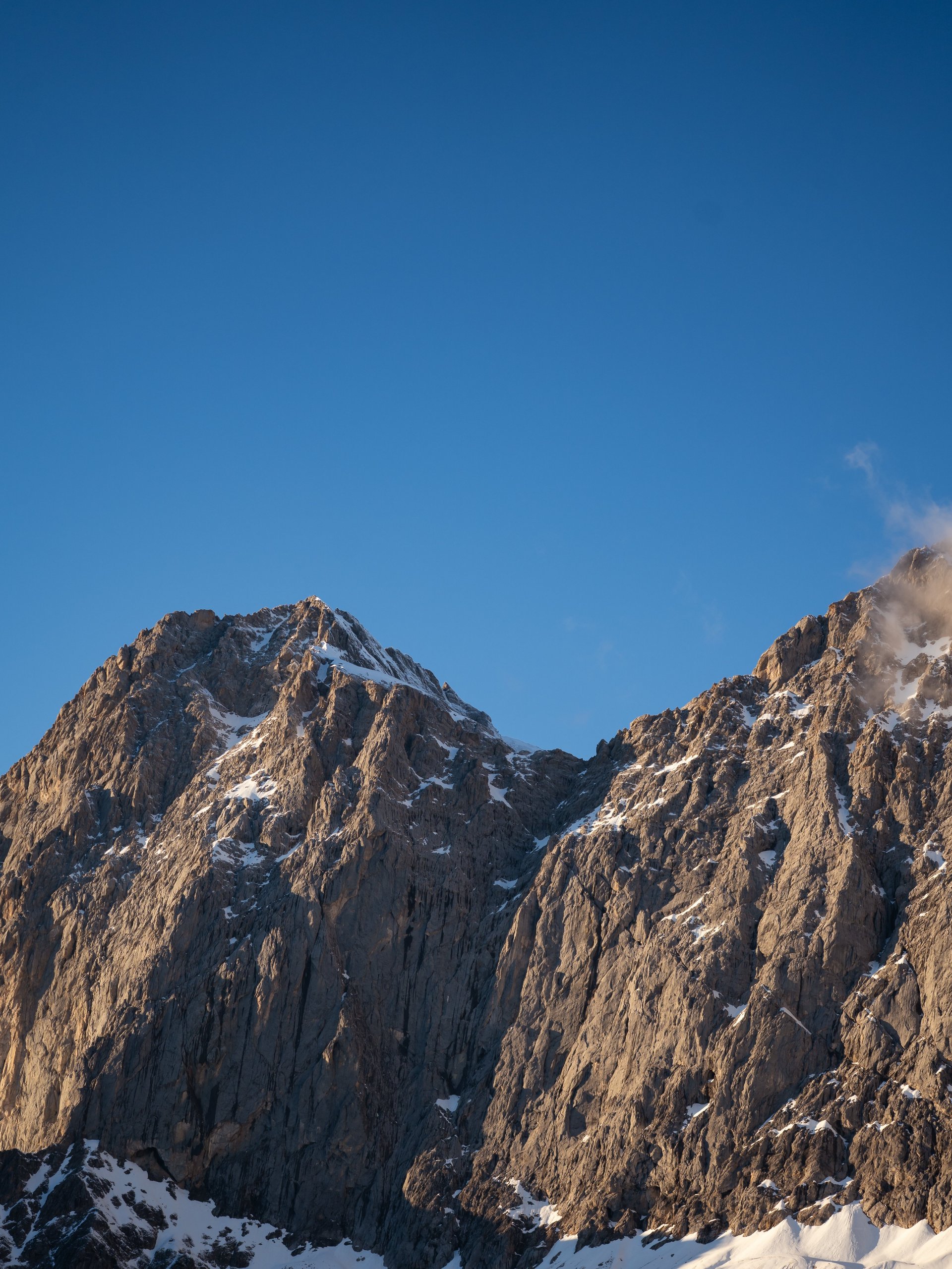 Rugged mountain range with snow-capped peaks and grassy slopes beneath a clear sky