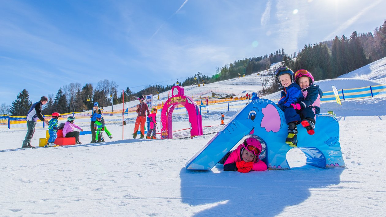 Winterspaß für die ganze Familie Kinder spielen im Schnee mit einem bunten Elefanten-Spielgerät und beim Skifahren