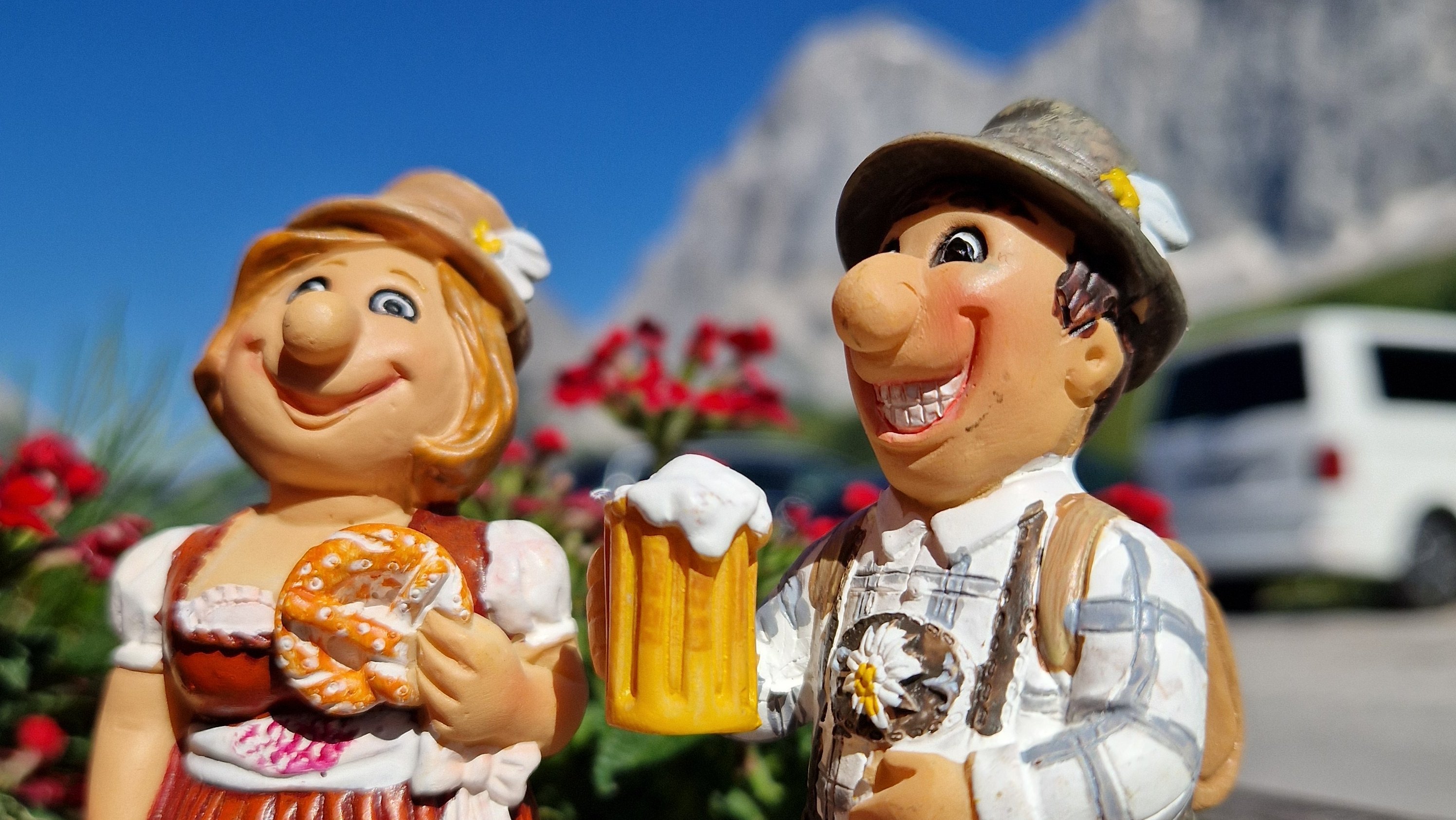 Traditionelle Figuren mit Bier und Brezel Zwei bunte Figuren in Tracht, eine mit Bierkrug und die andere mit Brezel, vor natürlicher Kulisse
