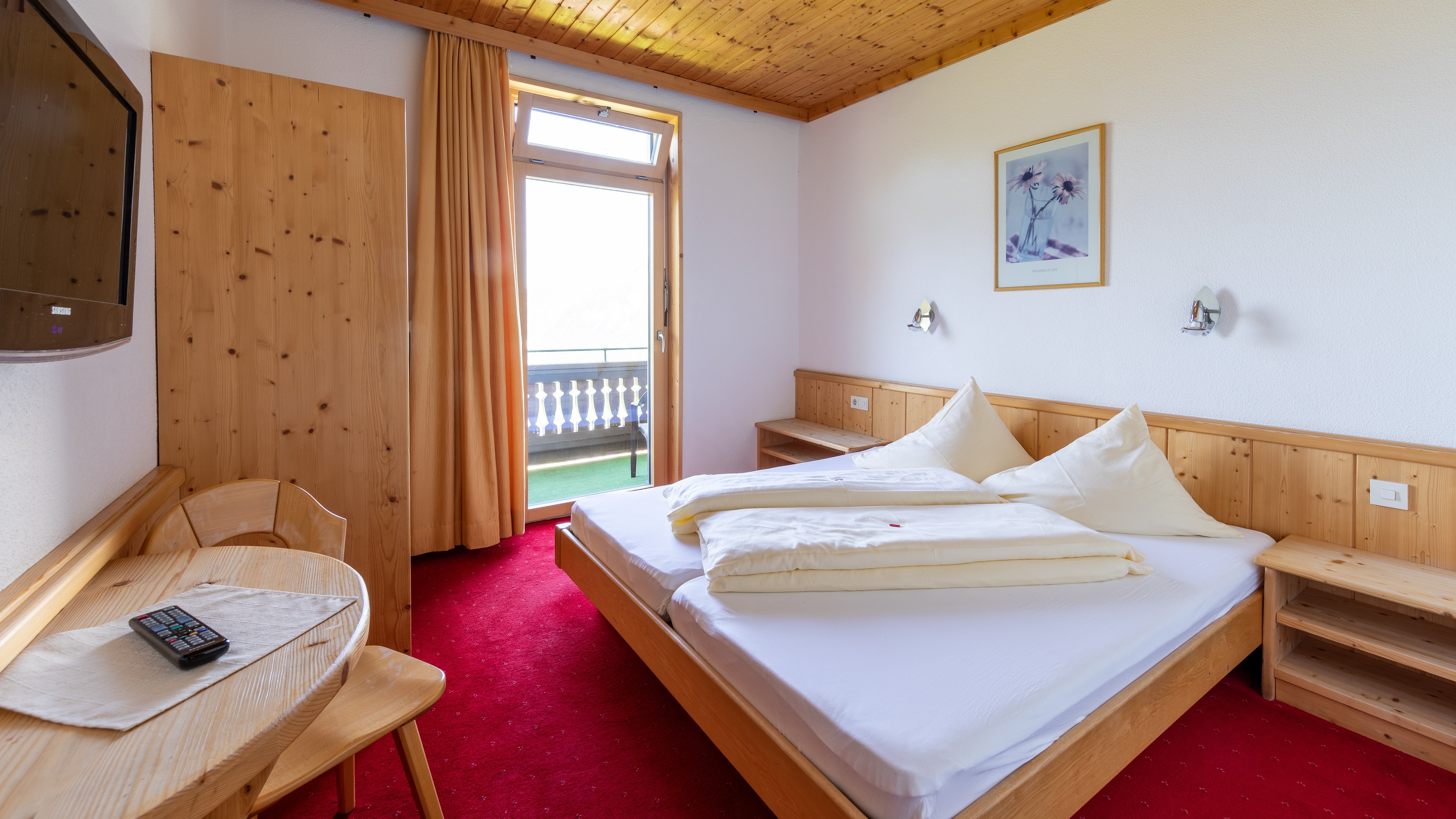 Hotelzimmer mit Doppelbett und Holzmöbeln, Zugang zum Balkon mit Ausblick nach draußen.