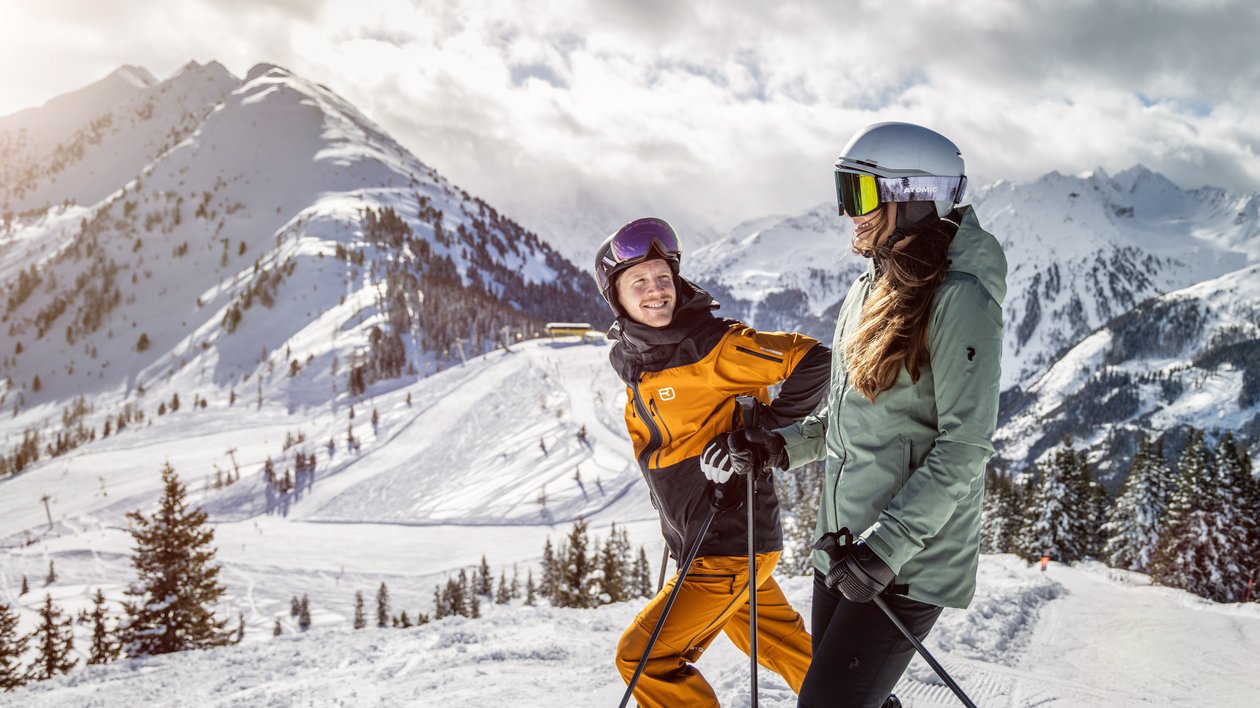 Two skiers navigating a snowy mountain slope with majestic peaks in the background