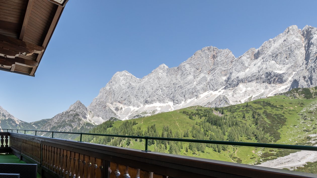 Alpine Aussicht vom Balkon Balkon mit Stuhl und Blick auf eine Berglandschaft unter blauem Himmel in den Alpen