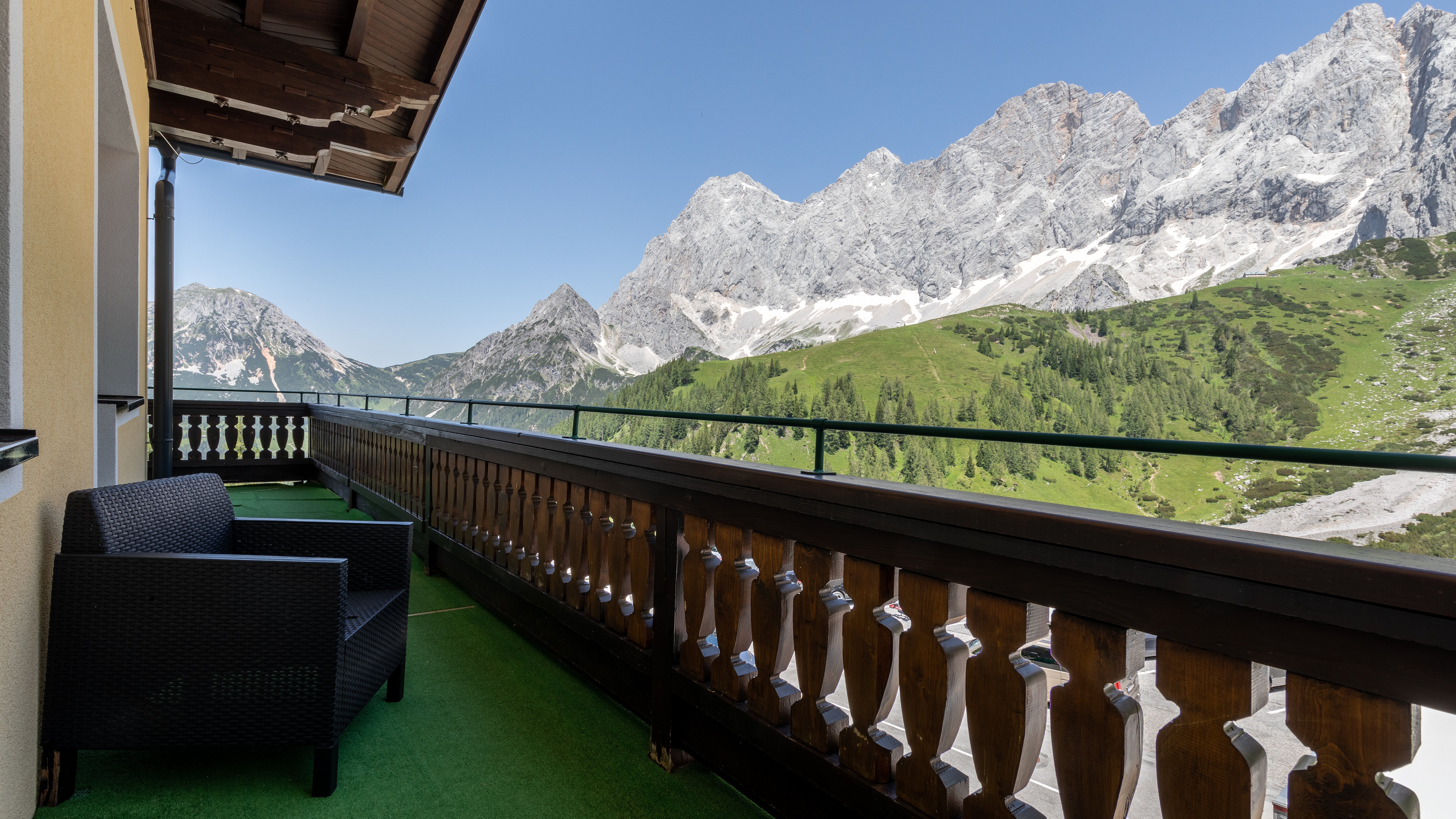 Balkon mit Stuhl und Blick auf eine Berglandschaft unter blauem Himmel in den Alpen