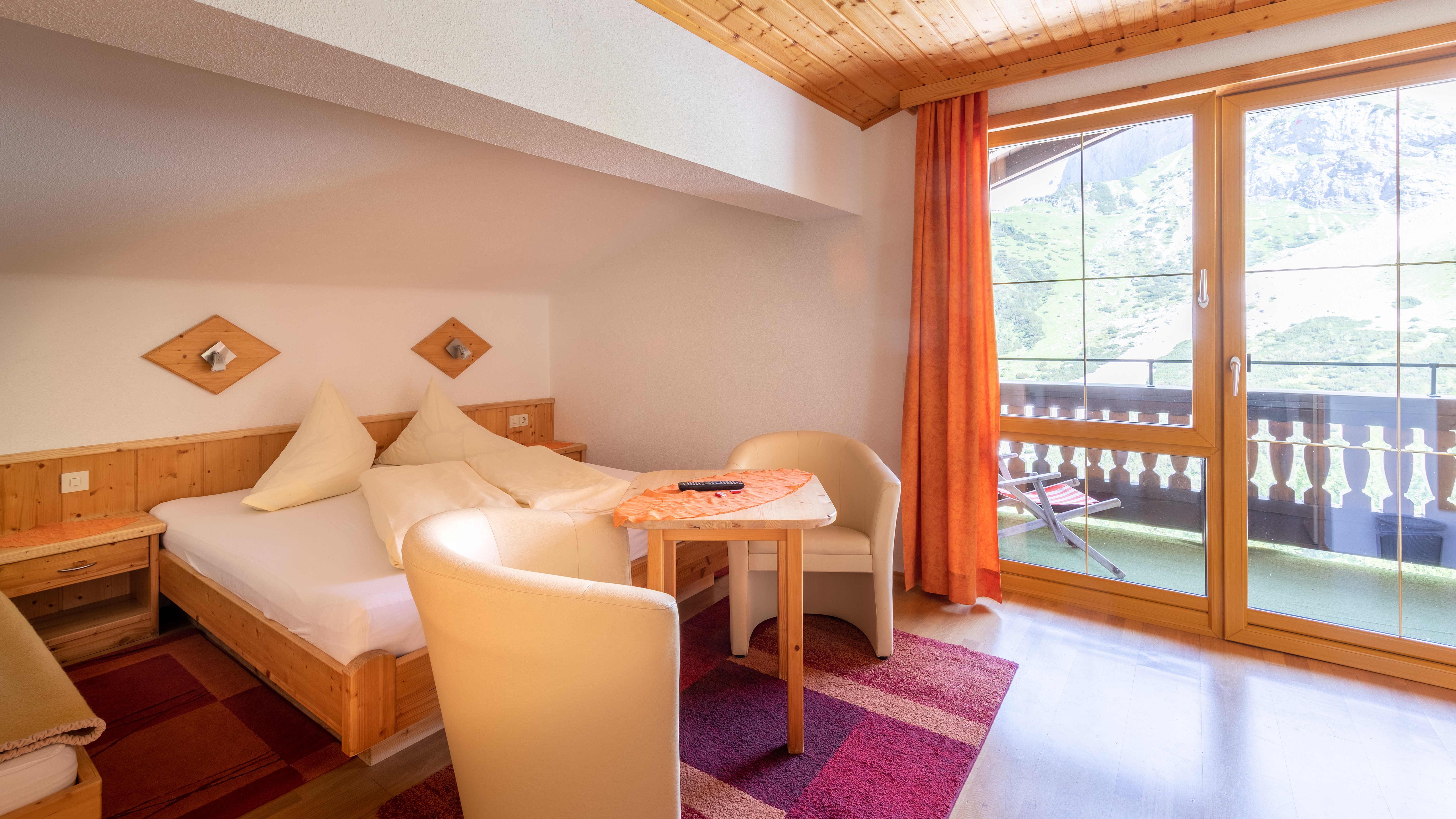 Hotelzimmer mit Holzdekor, Tisch und Stühlen sowie Balkon mit Ausblick auf die Berge