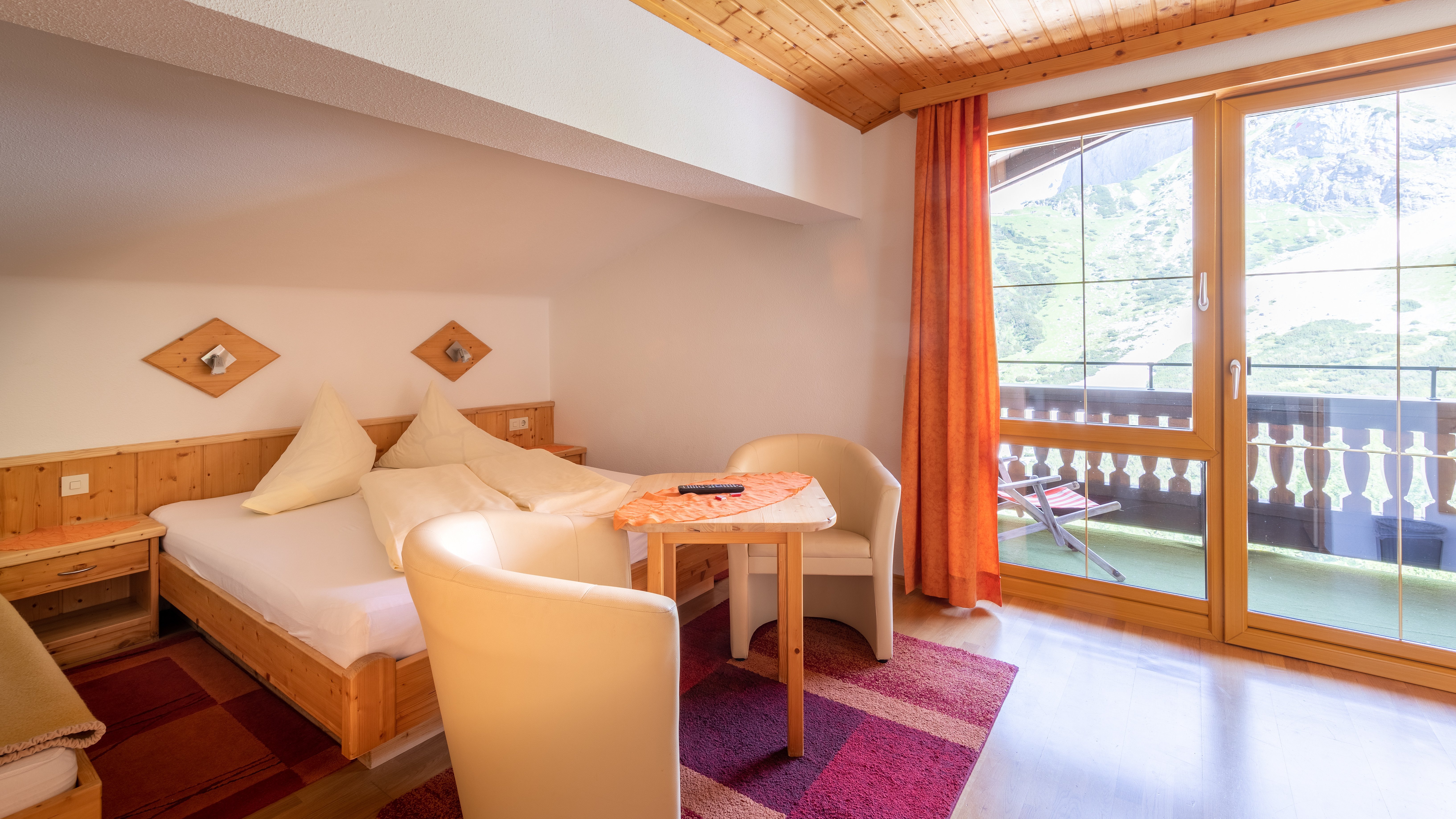 Hotelzimmer mit Holzdekor, Tisch und Stühlen sowie Balkon mit Ausblick auf die Berge